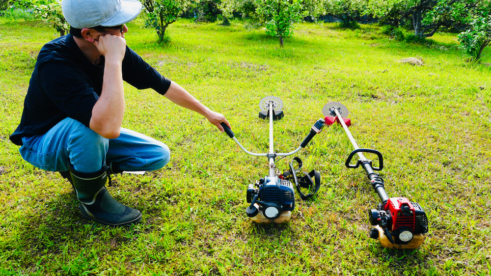 畑で古い草刈り機2台を見て買い替えを検討している様子
